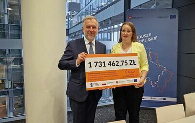 Dwie osoby trzymają w rękach symboliczny czek na kwotę 1,7 mln zł.