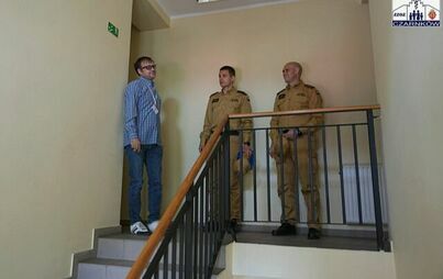 Trzech mężczyzn, w tym dwóch strażaków rozmawiają na klatce schodowej